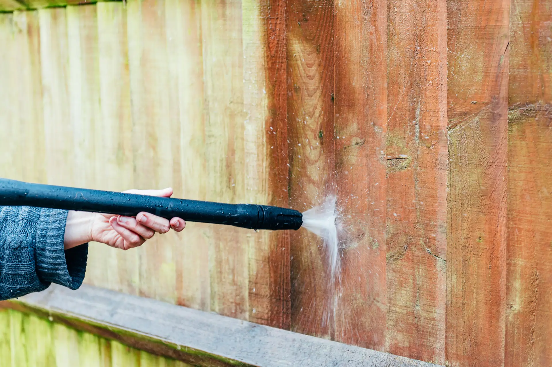 Pressure washer spray cleaning weathered wooden fence boards.