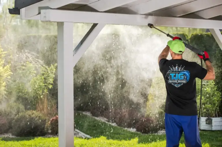 Worker wearing a black TJG shirt washing the roof of a covered patio.