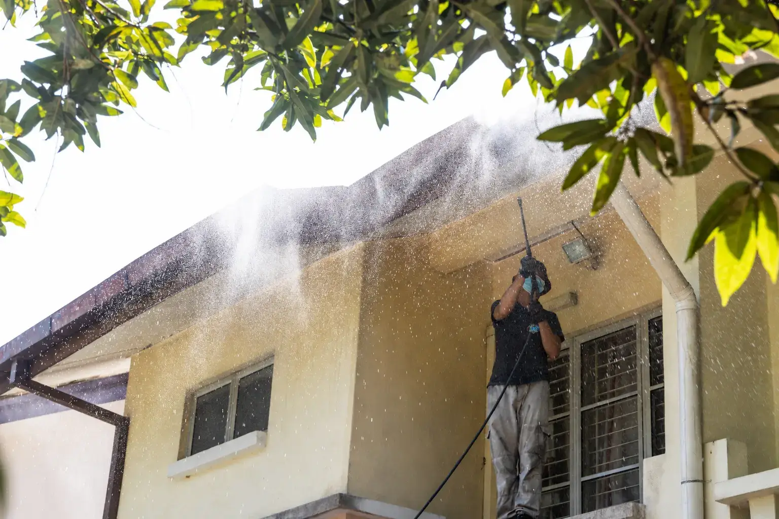 Worker pressure washing house eaves while wearing a black TJG shirt.