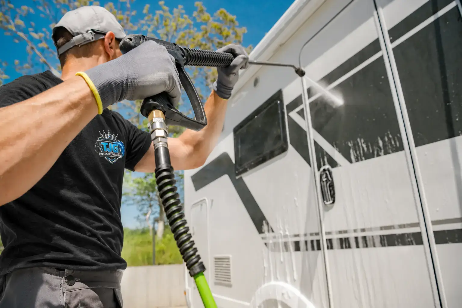 Worker in a black TJG shirt washing the side of an RV.