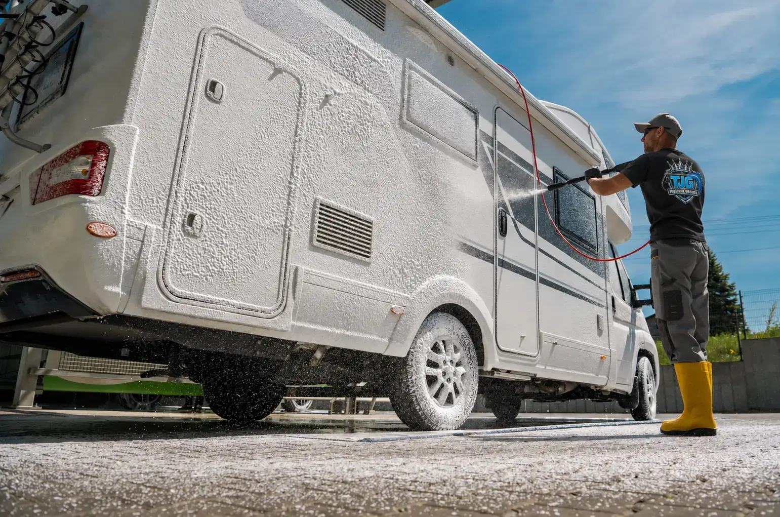 Worker wearing a black TJG shirt washing the exterior of an RV.
