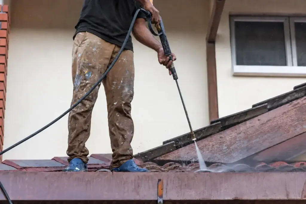 Worker using a pressure washer on a red tile roof.
